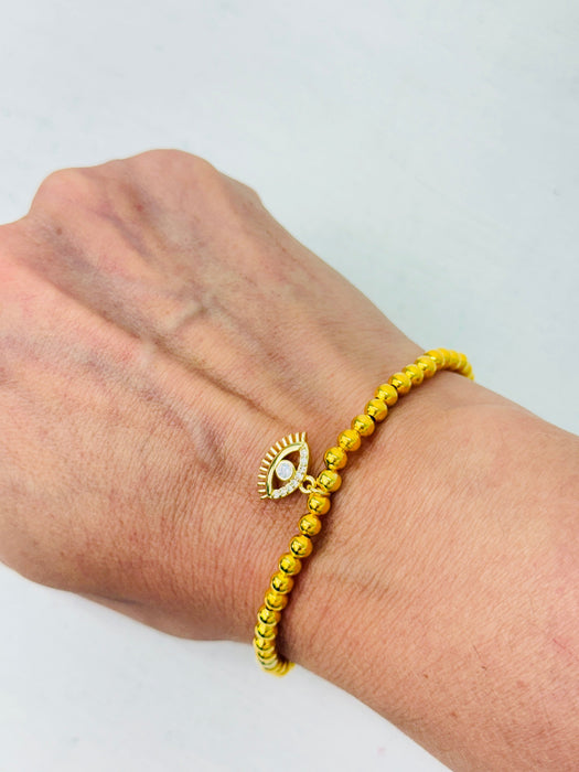 Gold beaded bracelet with an eye design on a wrist against a light background