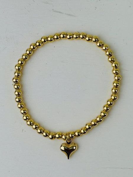 Gold beaded bracelet with a heart charm on a white background