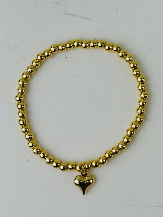 Gold beaded bracelet with a heart charm on a white background