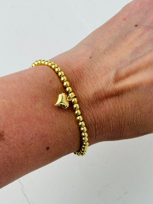 Gold beaded bracelet with a heart charm on a wrist against a white background