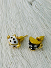 Pair of gold, black, and white teapot and tea cup-shaped earrings on a textured white background