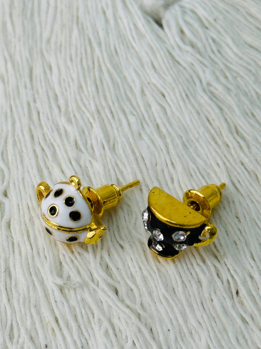 Pair of gold, black, and white teapot and tea cup-shaped earrings on a textured white background