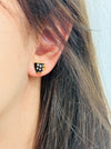 Close-up of an ear wearing a black and gold polka dot earring with blurred background