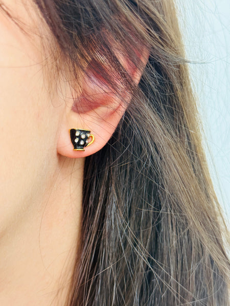 Close-up of an ear wearing a black and gold polka dot earring with blurred background