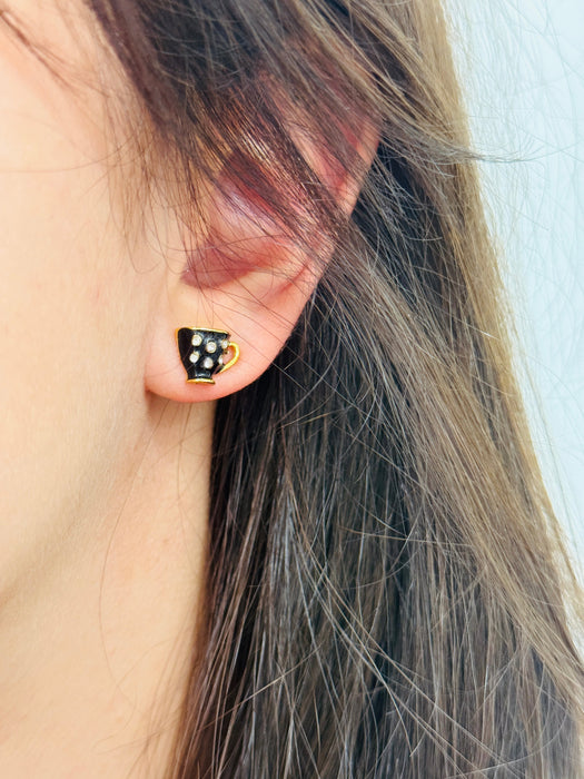 Close-up of an ear wearing a black and gold polka dot earring with blurred background