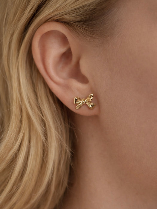 Gold bow-shaped earrings worn by a person with blonde hair.