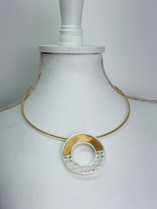 Necklace with a gold and silver circular pendant on a mannequin bust 
