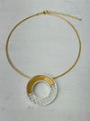 Gold-tone necklace with a round geometric pendant on a light background.