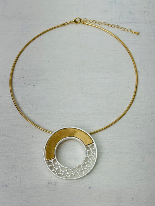 Gold-tone necklace with a round geometric pendant on a light background.