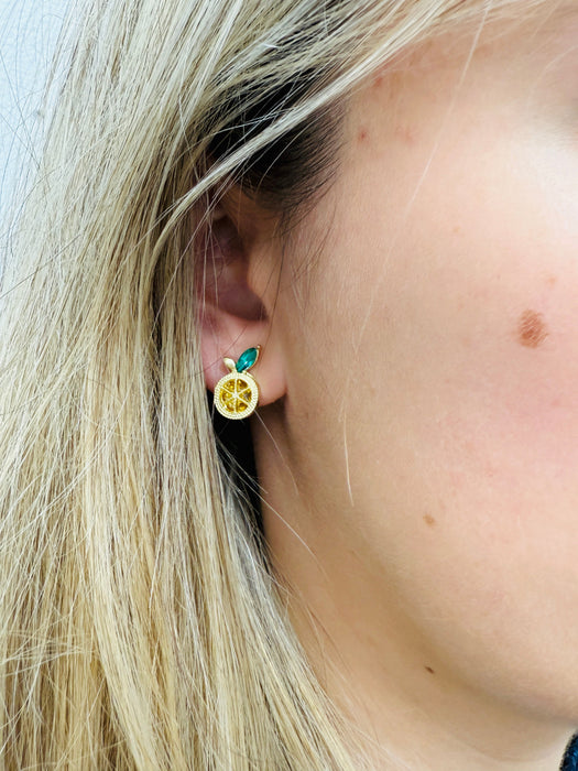 Close-up of a person wearing a gold citrus earring with green accents.