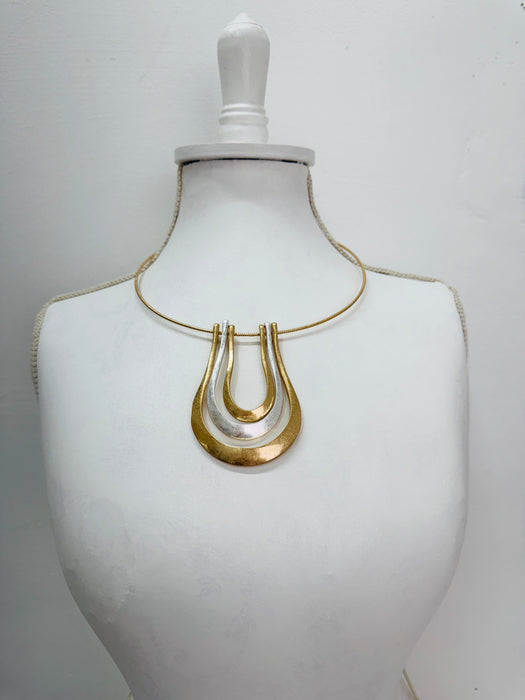 gold collar necklace with a triple-layered horseshoe-shaped metal pendant, displayed on a mannequin