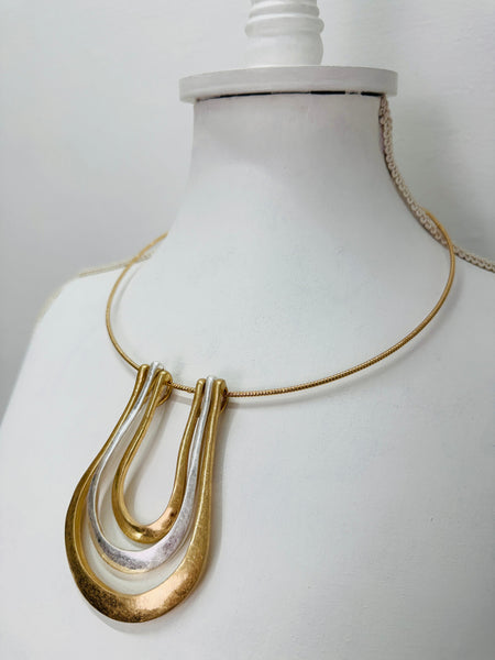 close-up gold collar necklace with a triple-layered horseshoe-shaped metal pendant
