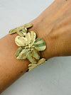 A gold-coloured cuff bracelet with floral details, worn on a person's wrist.