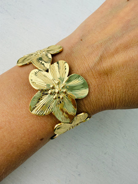 A gold-coloured cuff bracelet with floral details, worn on a person's wrist.