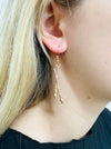 A pair of gold-colored earrings featuring a paint palette and paintbrush design.