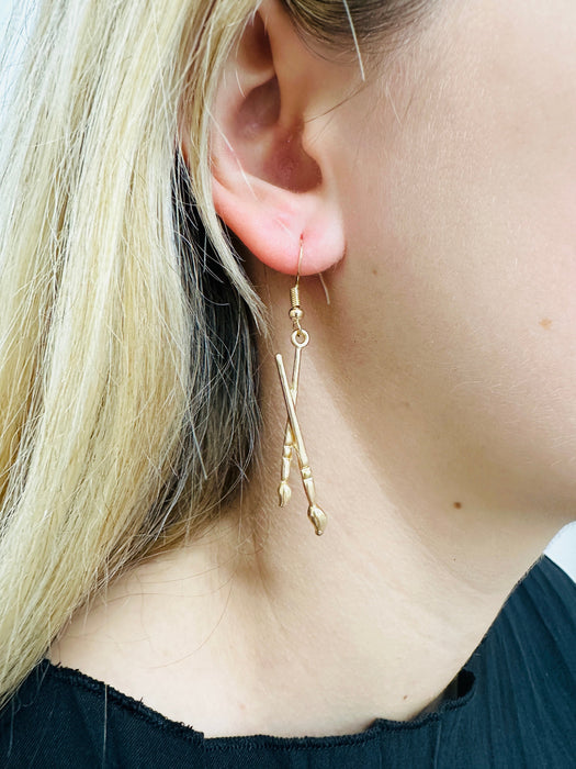 A pair of gold-colored earrings featuring a paint palette and paintbrush design.