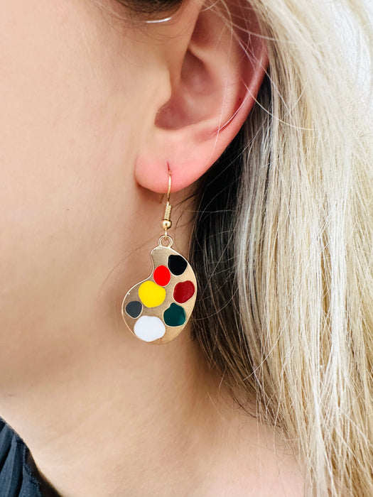 A pair of gold-colored earrings featuring a paint palette and paintbrush design.