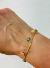Gold bracelet with colorful flower charms on a wrist against a white background