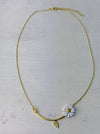 Gold necklace with a white flower pendant on a light gray background