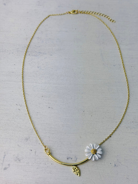 Gold necklace with a white flower pendant on a light gray background