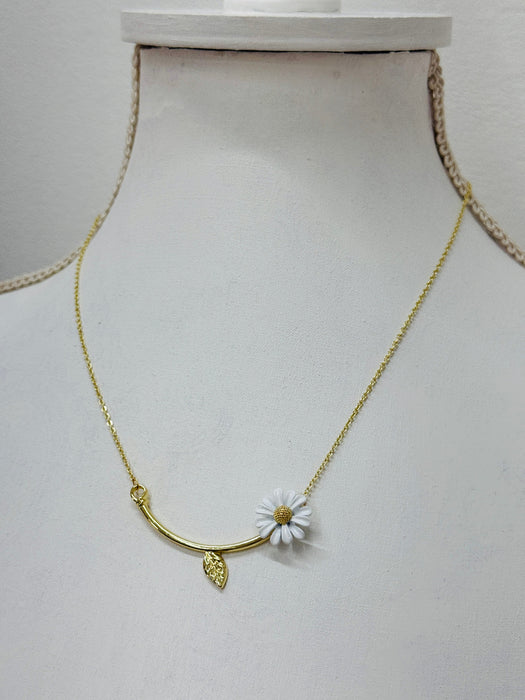 A gold-colored necklace with a daisy flower pendant and a tiny leaf detail, displayed on a mannequin.