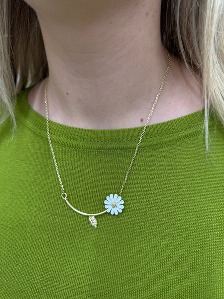 Necklace with a blue flower pendant worn by a person on a green shirt