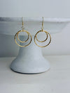 Gold hoop earrings on a white pedestal against a light gray background
