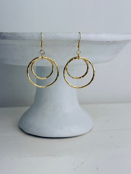 Gold hoop earrings on a white pedestal against a light gray background