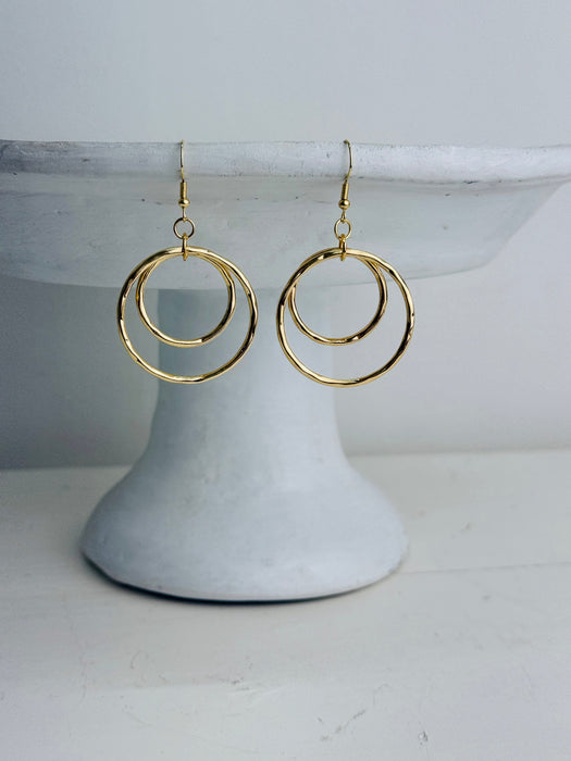 Gold hoop earrings on a white pedestal against a light gray background