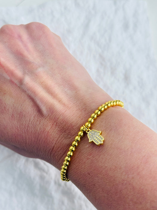 Gold beaded bracelet with a hamsa hand charm on a wrist against a white background