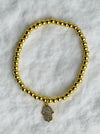 Gold beaded bracelet with a hamsa charm on a white marble background