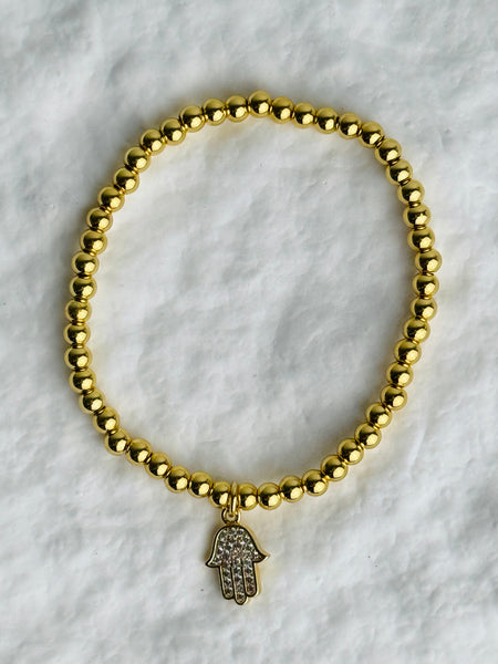 Gold beaded bracelet with a hamsa charm on a white marble background