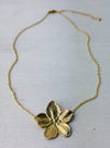 A gold-coloured necklace with a floral detail pendant, displayed on a light background.