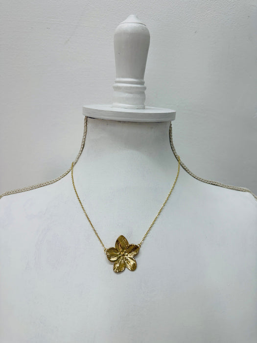 A gold-coloured necklace with a floral detail pendant, displayed on a mannequin