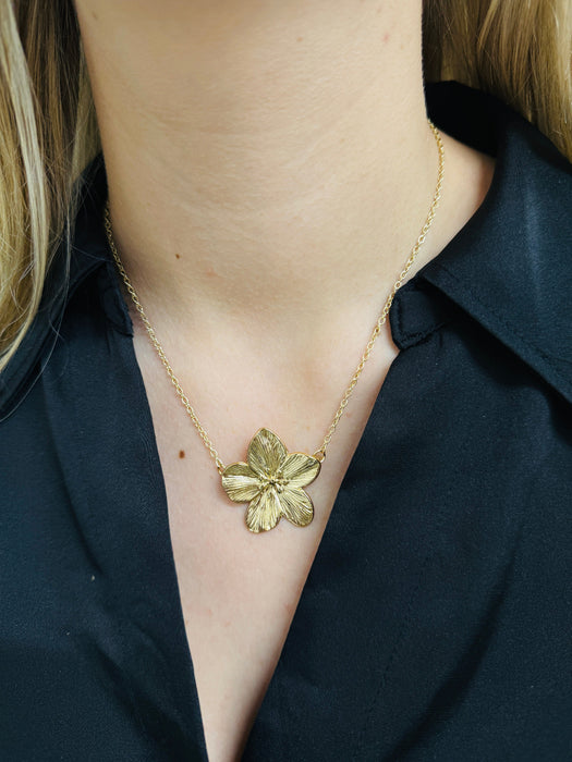 A gold-coloured necklace with a floral detail pendant, displayed on a model