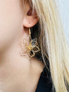 A close-up of a gold-coloured floral design dangle earring.