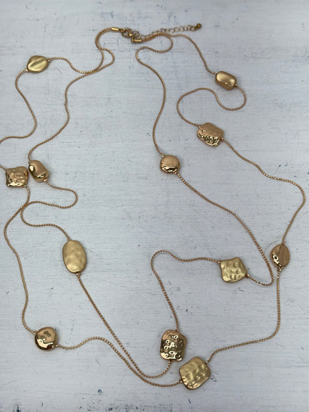 Long gold necklace with textured geometric charms displayed on mannequin