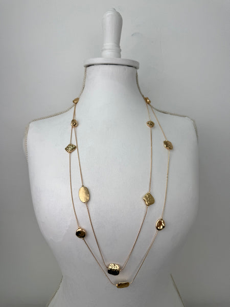 Long gold necklace with textured geometric charms displayed on mannequin