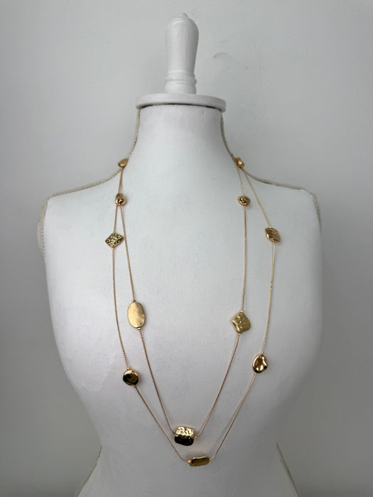 Long gold necklace with textured geometric charms displayed on mannequin