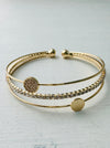 A gold-colored cuff bracelet with a mix of textured and smooth bands, displayed against a white background.