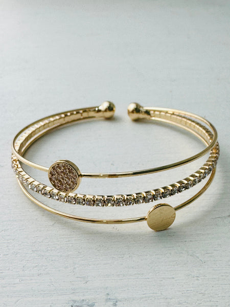 A gold-colored cuff bracelet with a mix of textured and smooth bands, displayed against a white background.