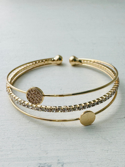 A gold-colored cuff bracelet with a mix of textured and smooth bands, displayed against a white background.