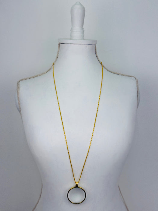 Gold magnifying glass pendant necklace with round glass lens on a gold chain.