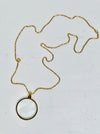 Gold magnifying glass pendant necklace with round glass lens on a gold chain, displayed on a white backgrond.