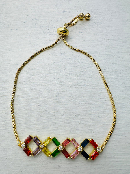 Multicolored gemstone bracelet on a gold chain against a light gray background