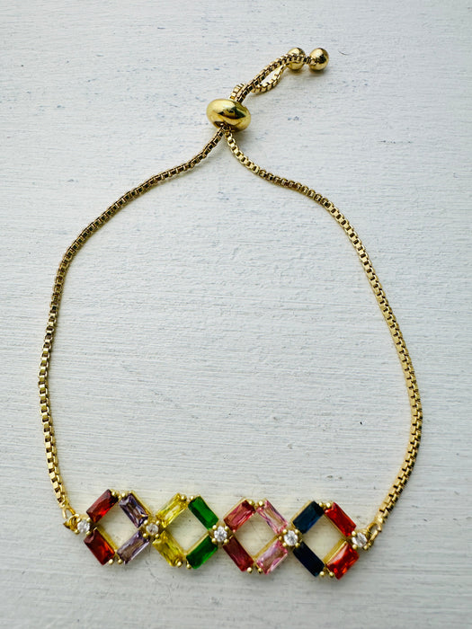 Multicolored gemstone bracelet on a gold chain against a light gray background