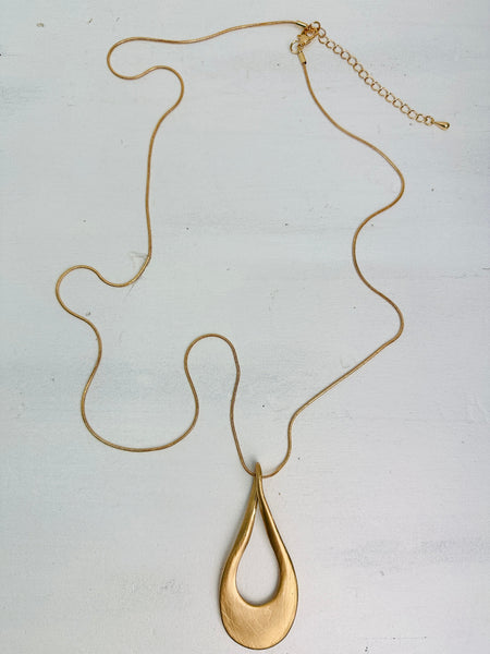 aerial view of gold necklace with a long chain and a teardrop-shaped metal pendant