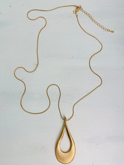 aerial view of gold necklace with a long chain and a teardrop-shaped metal pendant