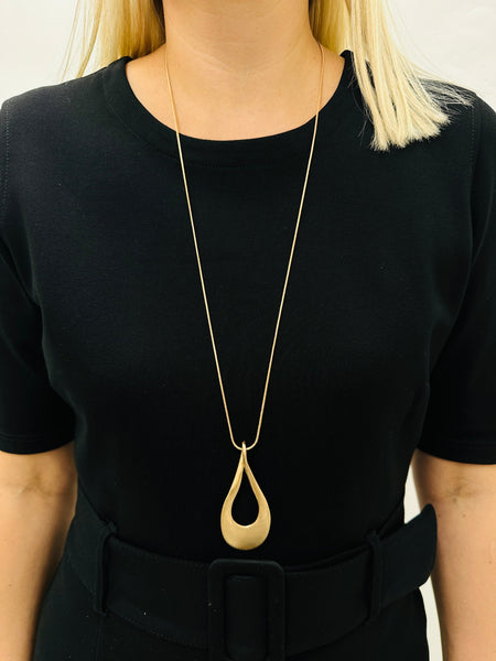 gold necklace with a long chain and a teardrop-shaped metal pendant, displayed on a model