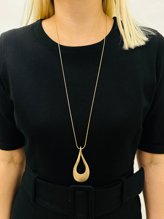 gold necklace with a long chain and a teardrop-shaped metal pendant, displayed on a model